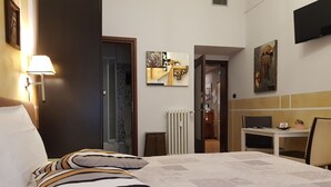A hotel room with a bed, a desk, and a chair. There is a lamp on the wall and a painting on the wall. - Cittadella (Verona)