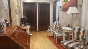 A hotel room with a wooden desk, a telephone, a small table with chairs, a red carpet, and a painting on the wall. - Cittadella (Verona)