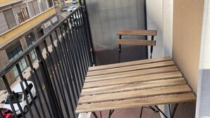 A balcony with a wooden table and bench, a metal railing, and a view of a street with parked cars. - Cittadella (Verona)