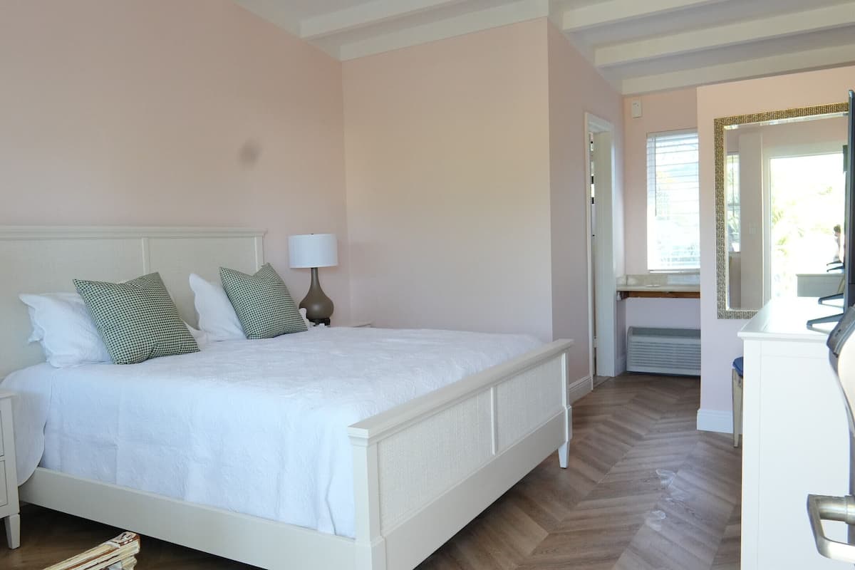 A neatly made bed with white bedding and two pillows, a bedside table with a lamp, and a dresser with a mirror.