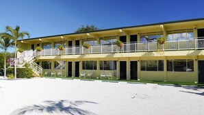 Un motel à deux étages avec un balcon à l’étage supérieur, des places assises à l’extérieur et un ciel dégagé.