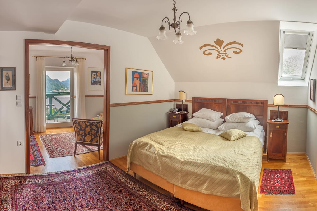 A bedroom with a large bed, a chandelier, and a view of a balcony.
