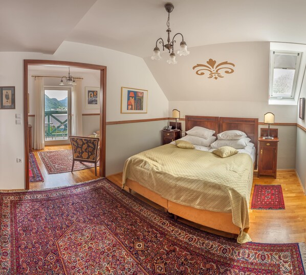 A bedroom with a large bed, a chandelier, and a view of a balcony.