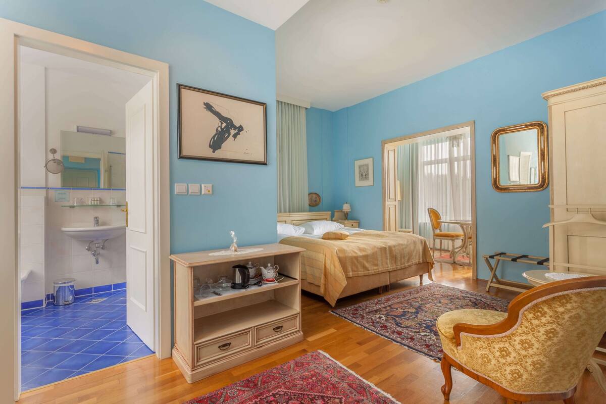 A bedroom with a bed, a dresser, a chair, a rug, and a bathroom with a sink and mirror.