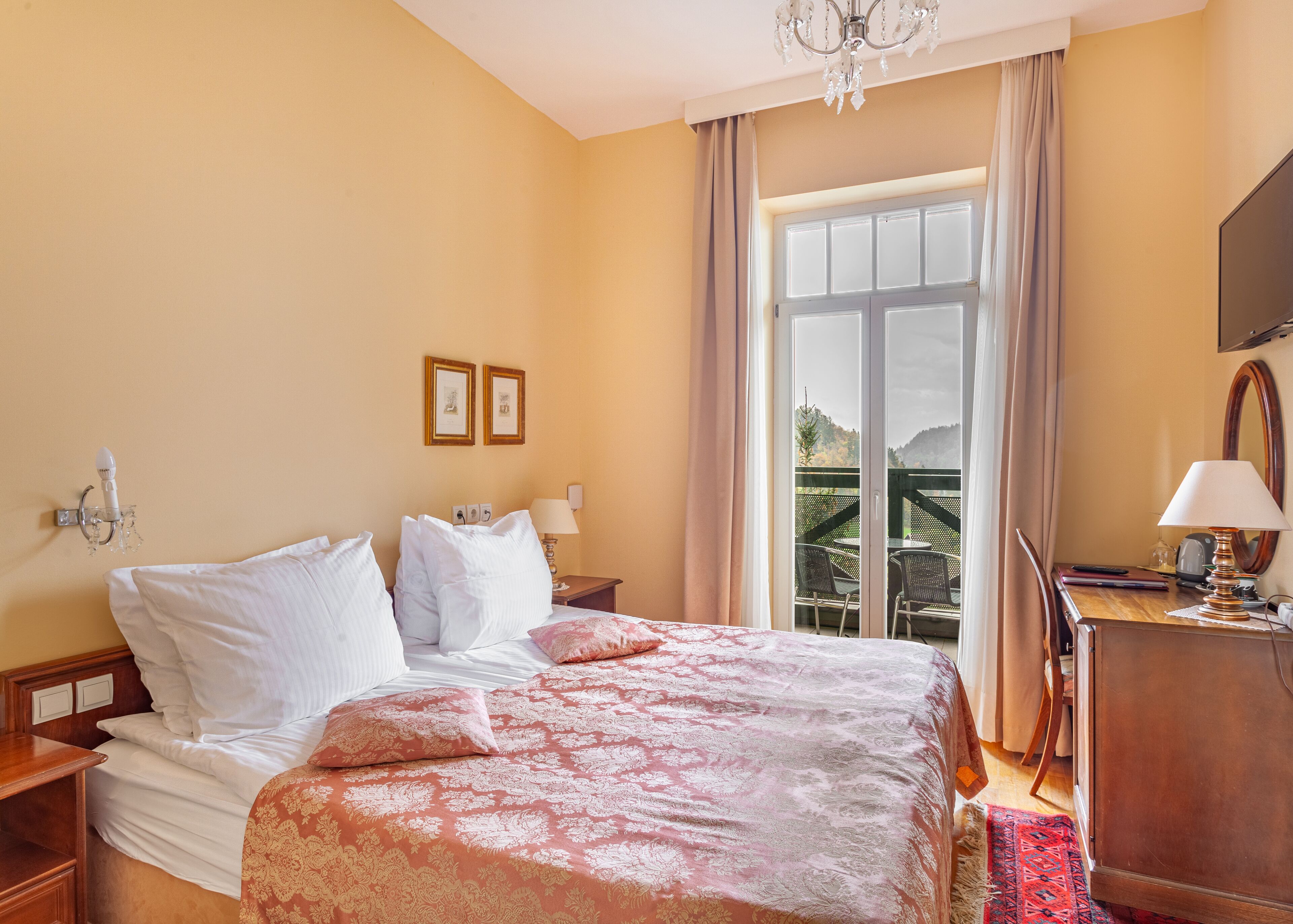 Habitación de hotel con cama, mesita de noche, cómoda, lámpara y vistas al exterior.