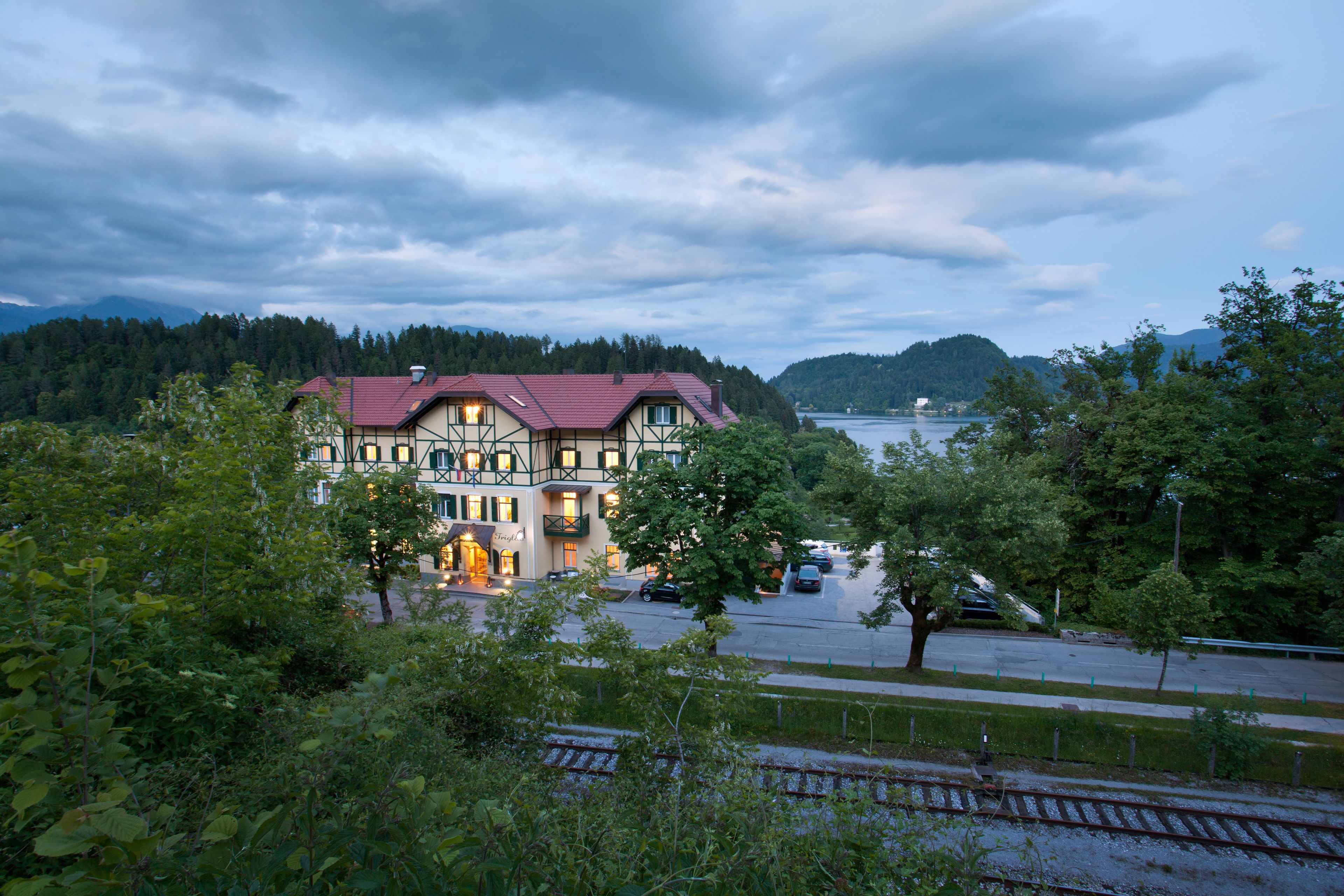 A traditional building with a red roof, surrounded by greenery and a body of water in the background.