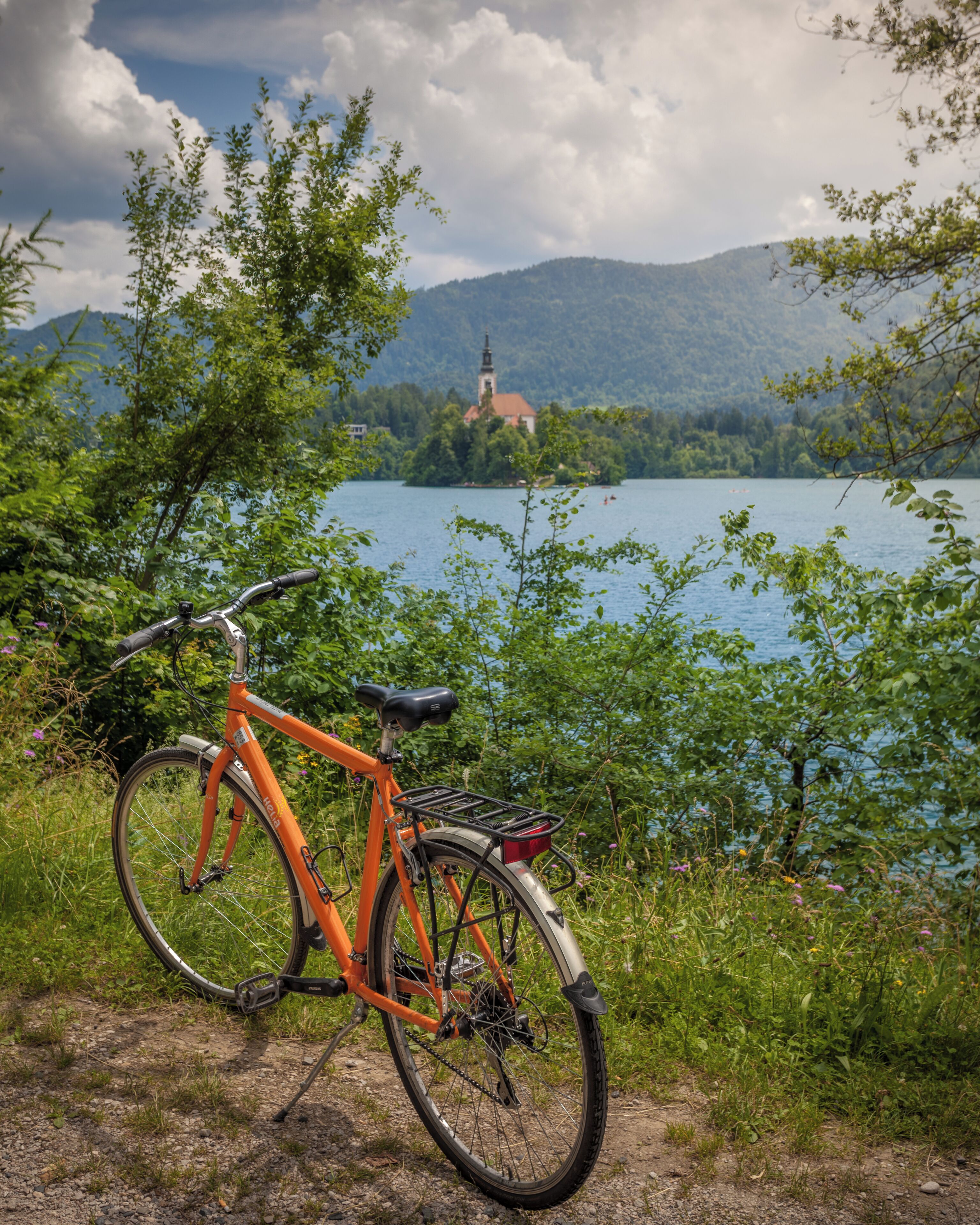A bicycle parked by a lakeside path with a church in the background.