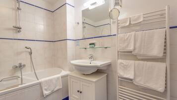 Un baño con bañera, lavamanos, espejo y toallero.
