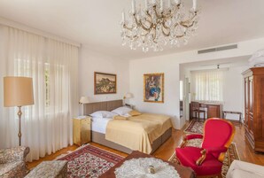 Un dormitorio con una cama, un sillón rojo, un escritorio de madera y una araña.