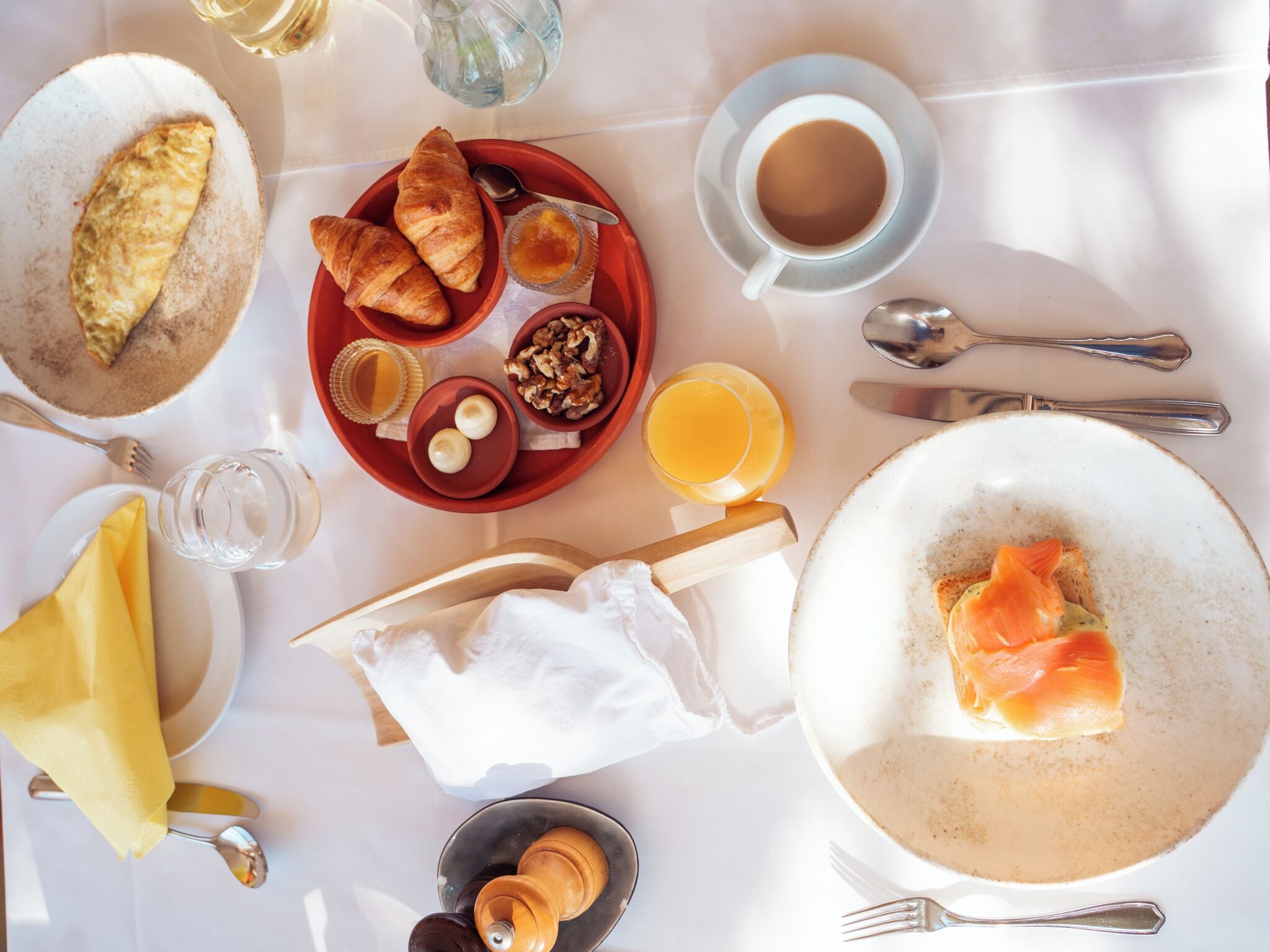 Un desayuno con cruasanes, huevos y salmón en platos, una taza de café y un vaso de zumo de naranja.