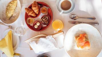 Un desayuno con cruasanes, huevos y salmón en platos, una taza de café y un vaso de zumo de naranja.