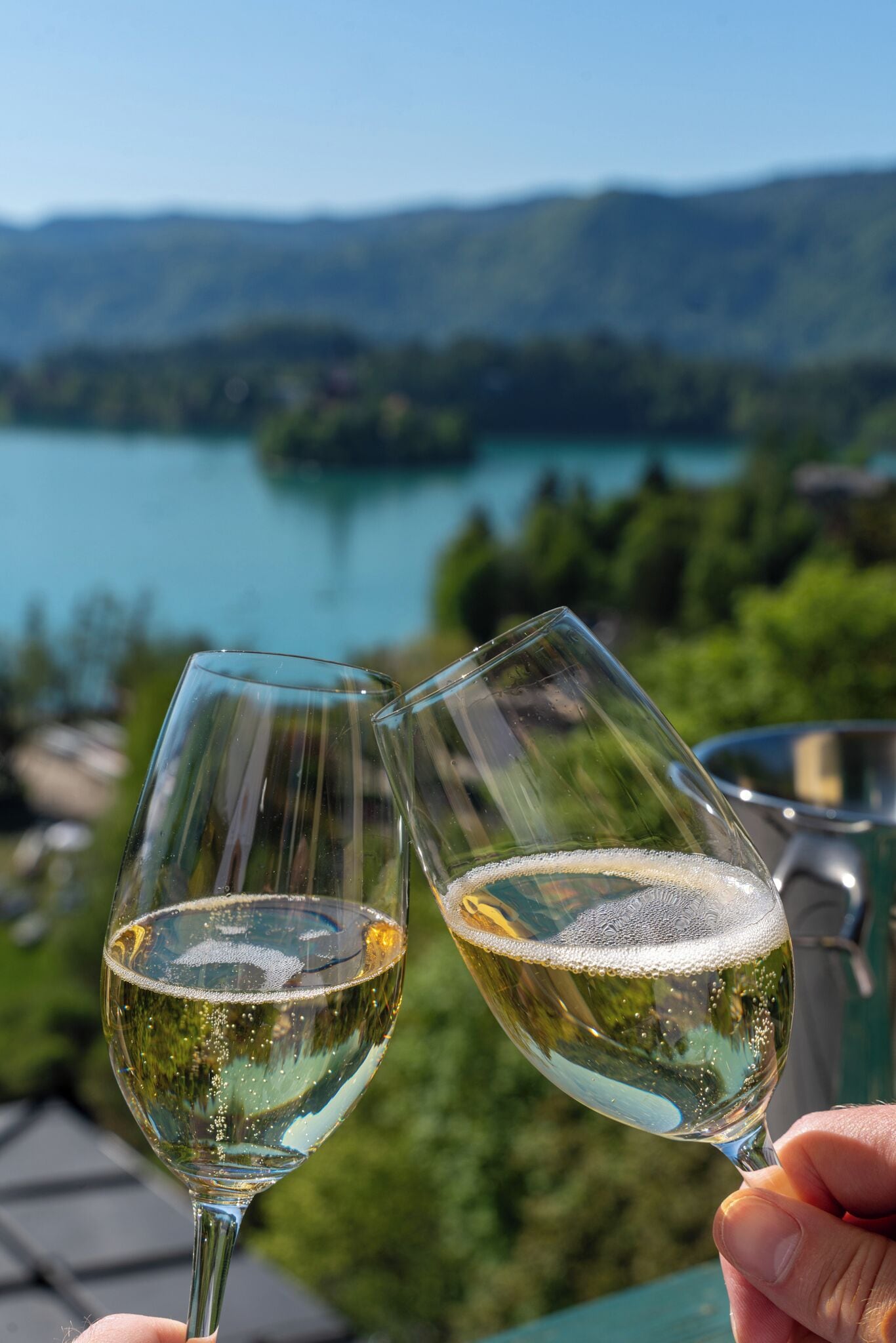 Two wine glasses held by a person with a scenic view of a lake and mountains in the background.