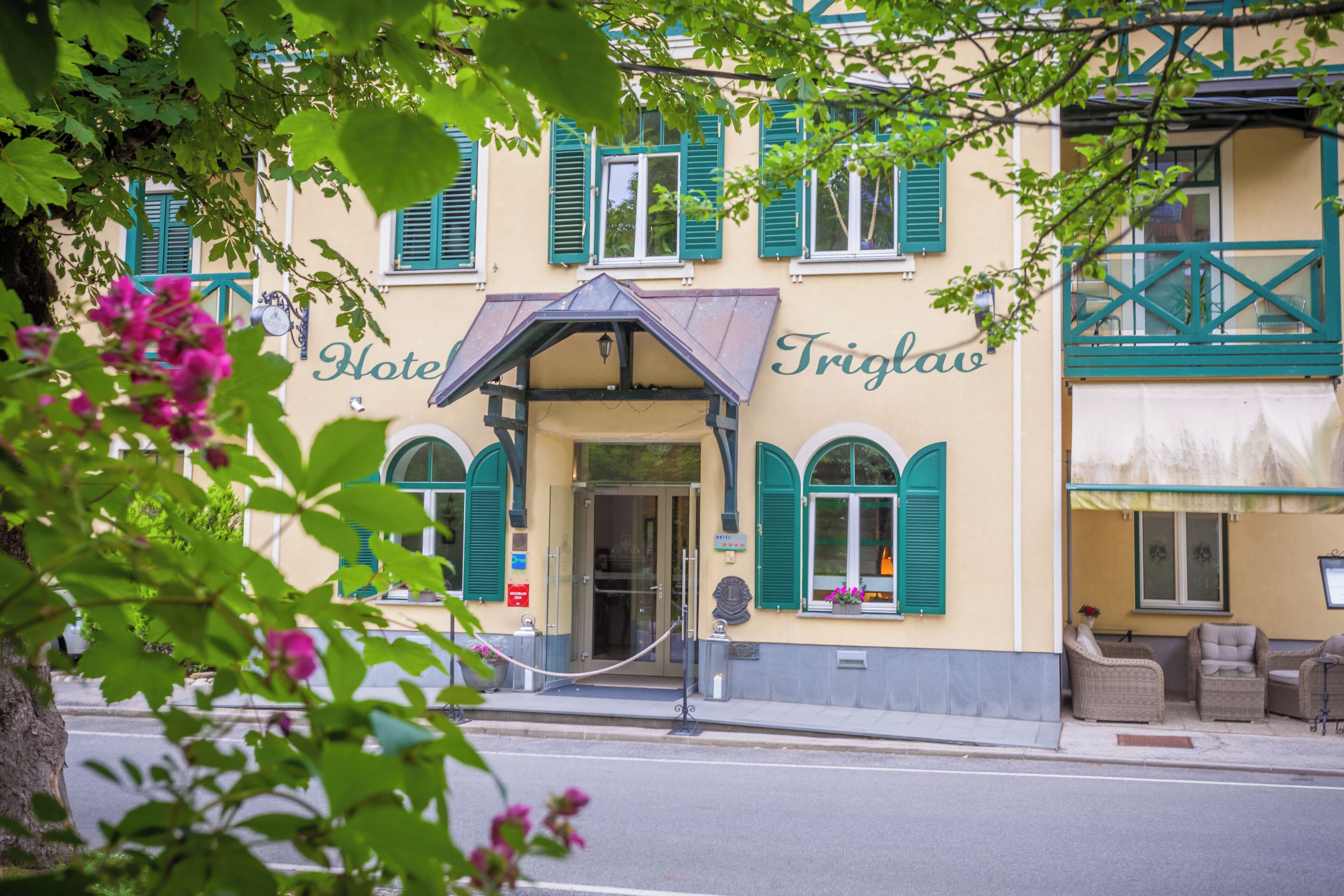 A hotel entrance with a covered porch, a sign reading 'Hotel Triglav,' and outdoor seating.