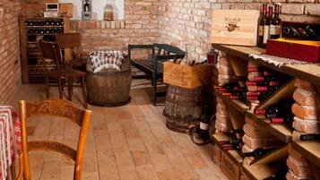 A rustic cellar with wooden shelves and barrels, a wooden table with a patterned tablecloth, and a chair.