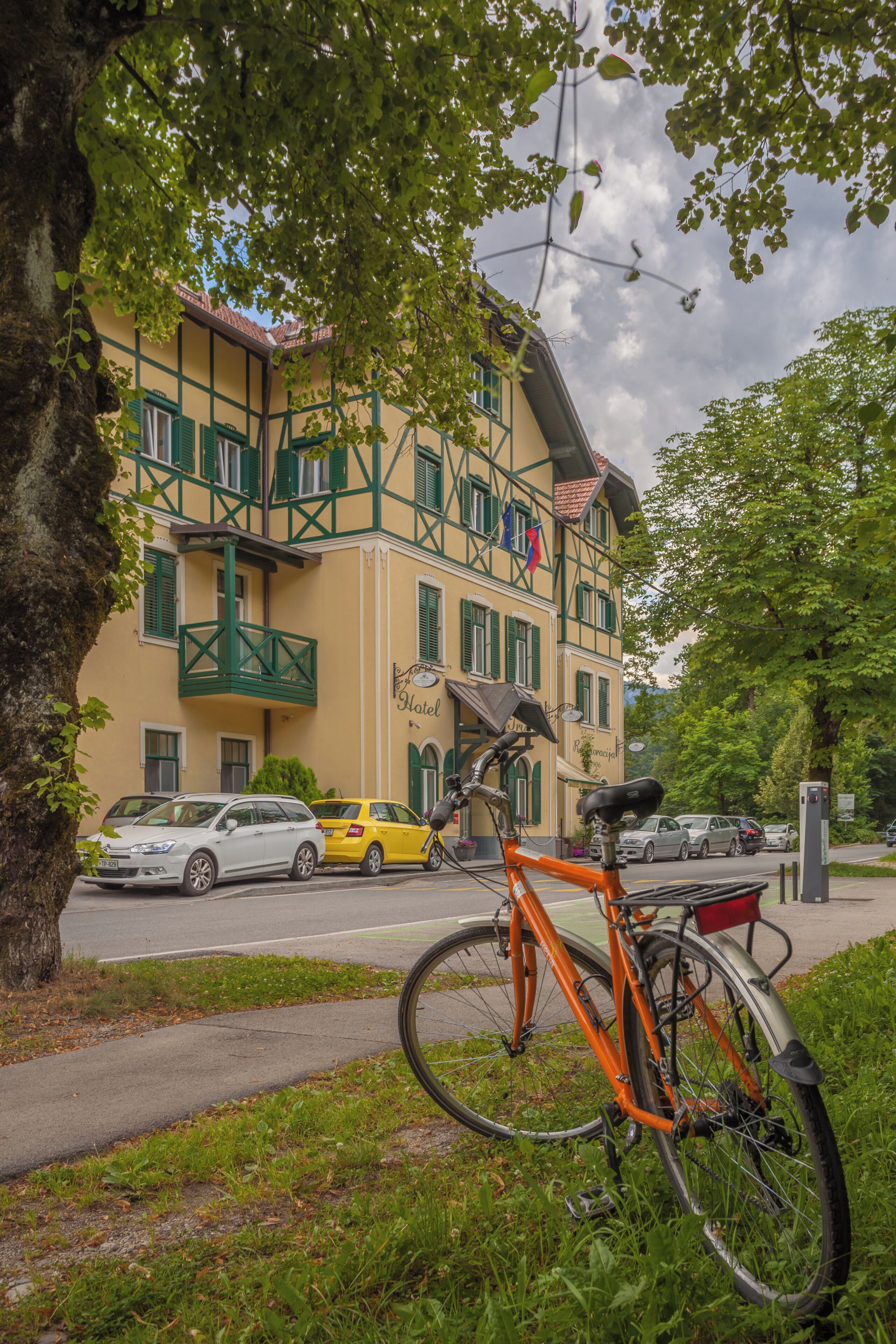 A hotel with a balcony, a bicycle parked in front, and cars parked on the street.
