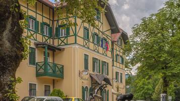 A hotel with a balcony, a bicycle parked in front, and cars parked on the street.