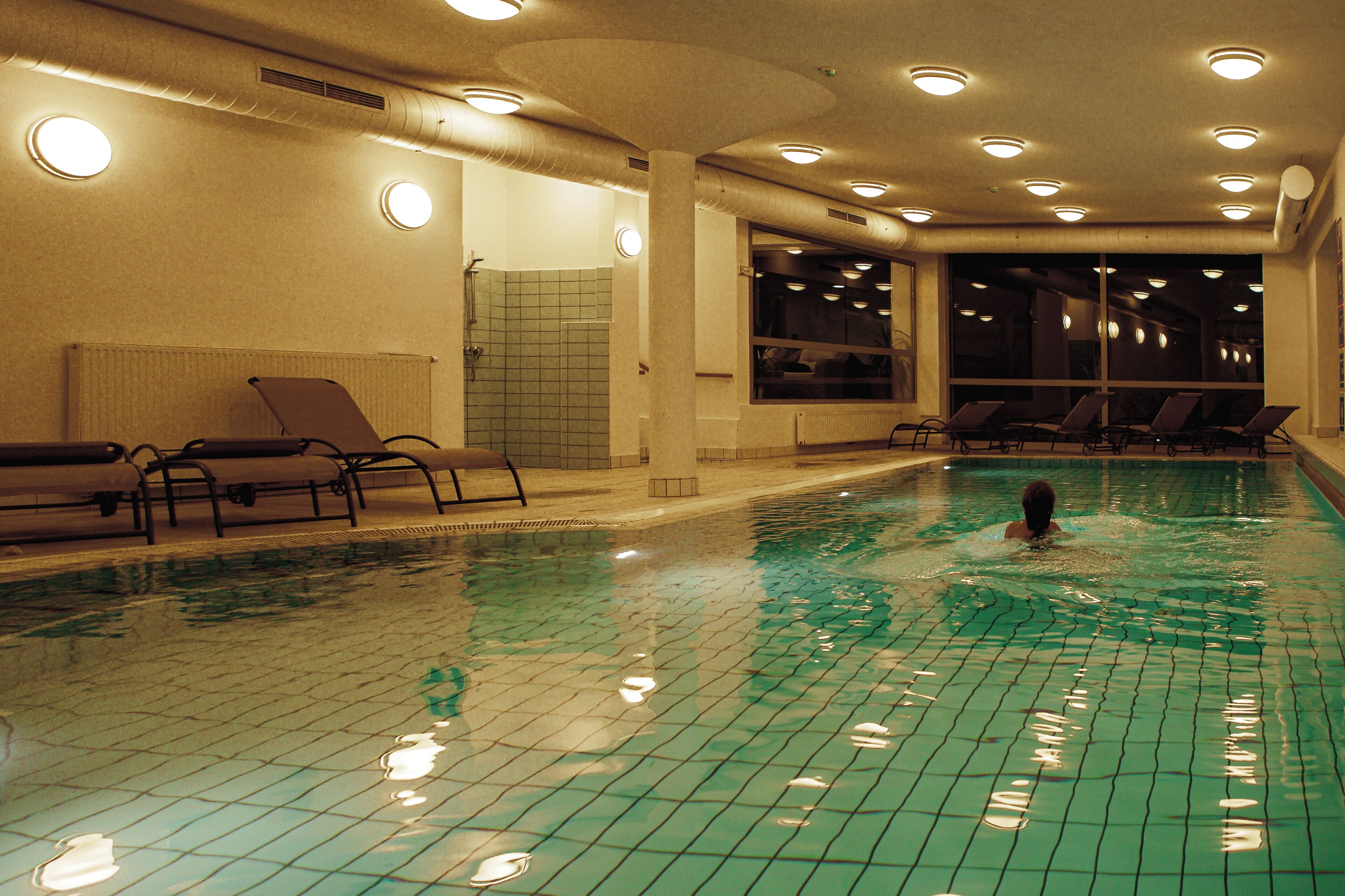 Una piscina interior amb parets de rajola, llums al sostre i gandules.