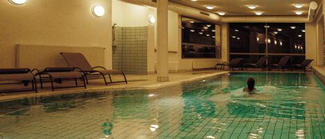 Una piscina interior amb parets de rajola, llums al sostre i gandules.