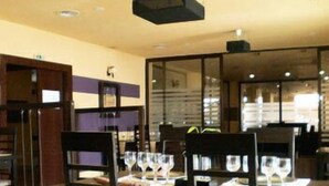 A restaurant interior with wooden chairs, tables set with wine glasses, and a modern ceiling design. - Maxim Oradea (Oradea)