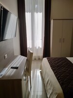 A hotel room with a bed, a desk with a TV, a chair, and a wardrobe.