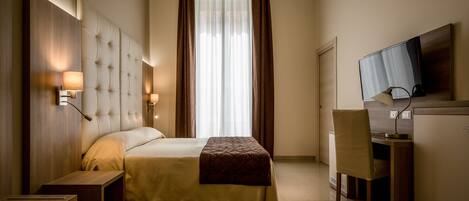A hotel room with a large bed, a desk, a chair, a television, and a window with curtains.