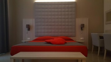 Een moderne hotelkamer met een groot bed, rode kussens, een nachtkastje, een bureau en een stoel.