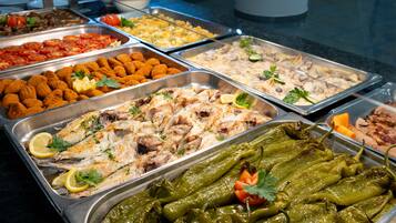 Un bufé con diversos platos, incluyendo pescado, verduras y otras comidas preparadas.