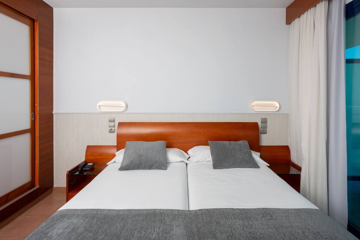 Quarto de hotel com uma cama grande, duas mesas de cabeceira, um telefone e um candeeiro fixado na parede.
