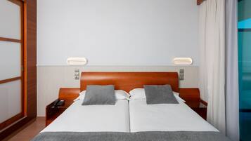 Una habitación de hotel con una cama grande, dos mesitas de noche, un teléfono y una lámpara fijada a la pared.