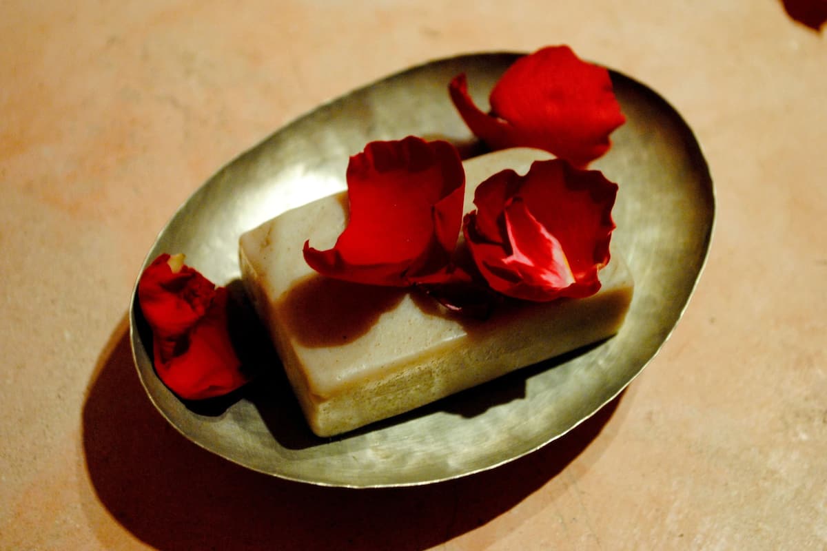 Un objeto rectangular sobre una superficie metálica redonda, con pétalos de rosa roja esparcidos alrededor.