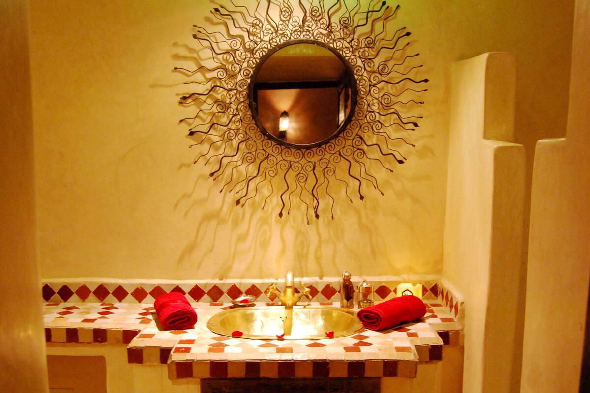 Un baño con un espejo decorativo, un lavabo con salpicadero de azulejos estampados y un perchero para toallas.