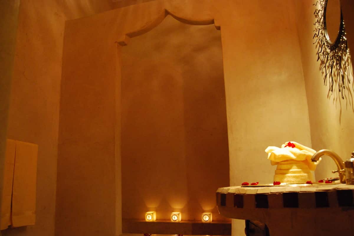 Un baño con un lavamanos, un perchero para toallas y tres velas encendidas en la pared.