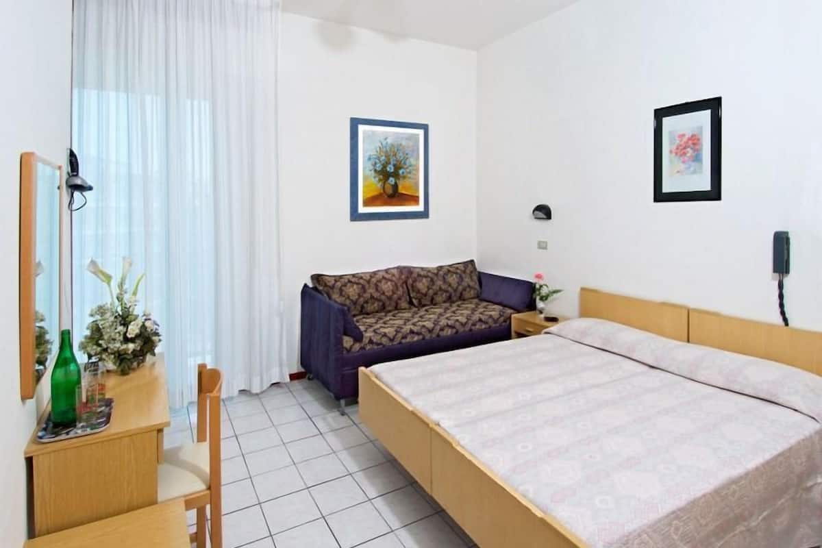 A bedroom with a bed, a sofa, a chair, a desk, and two framed pictures on the wall.
