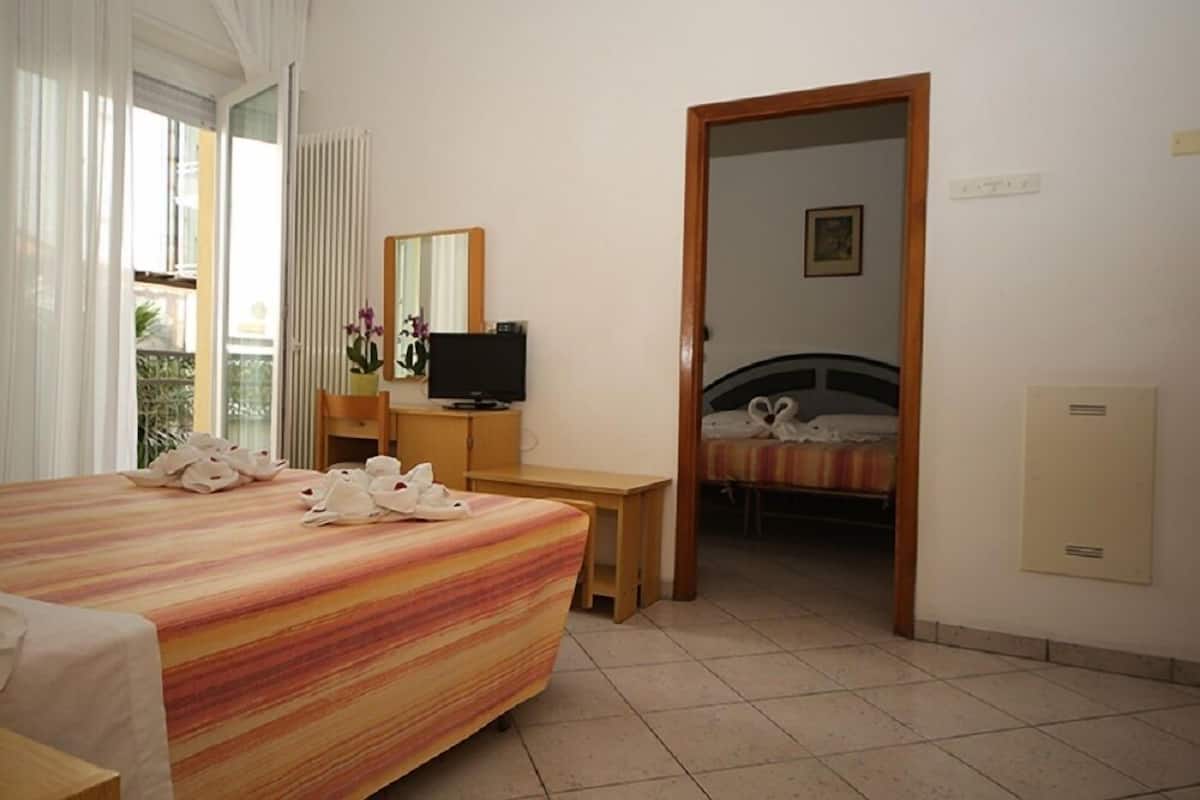 A hotel room with a bed, a desk, a television, and a bathroom visible through an open door.