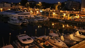 Un puerto deportivo al anochecer con barcos amarrados, un puente al fondo y edificios iluminados.