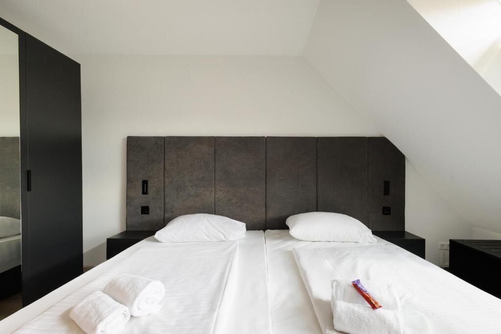 A modern hotel room with a large bed, two nightstands, and a dark headboard.