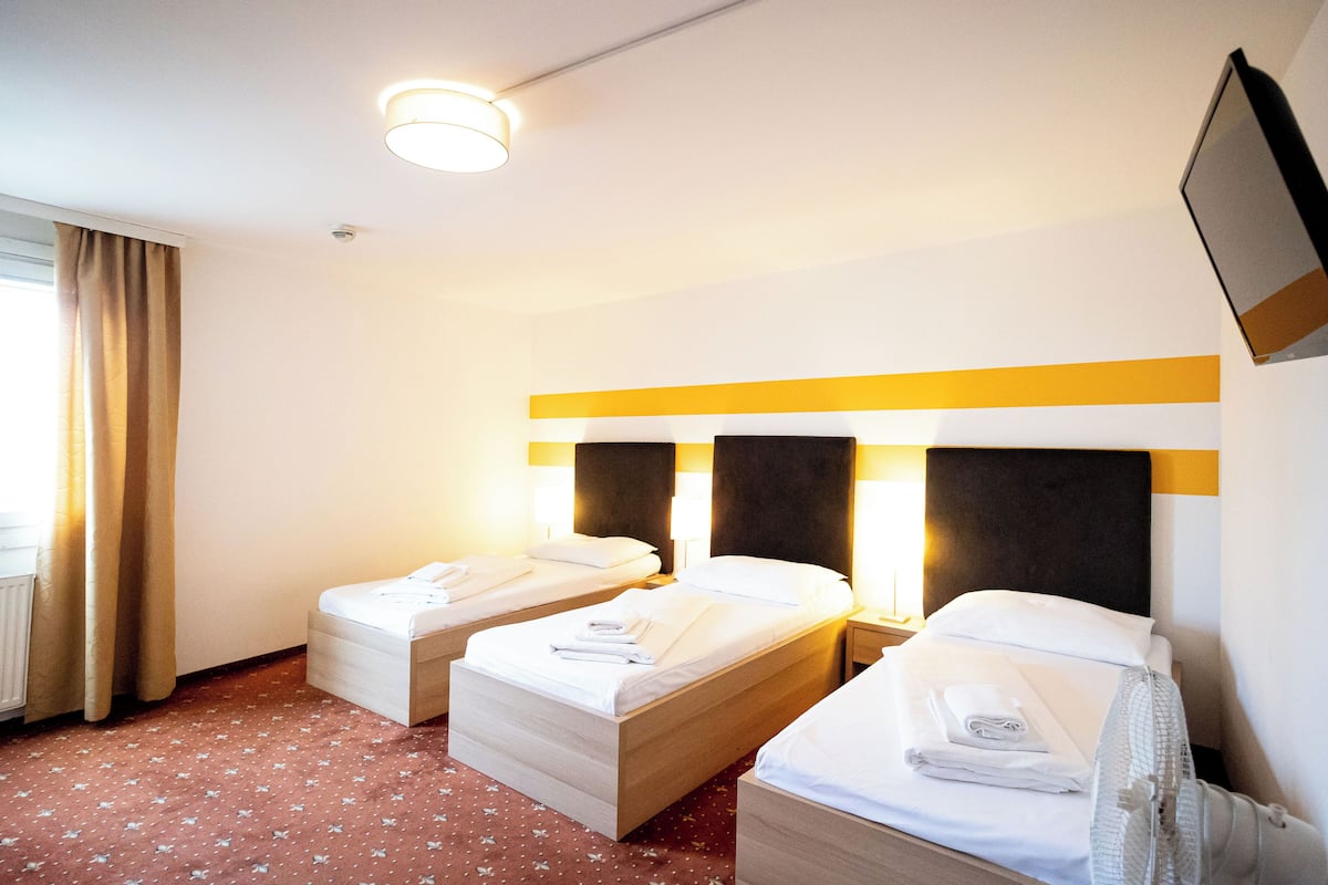 A hotel room with two beds, a flat-screen TV mounted on the wall, and a window with curtains.
