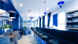 A bar area with blue seating, a counter with bottles, and hanging blue light fixtures.