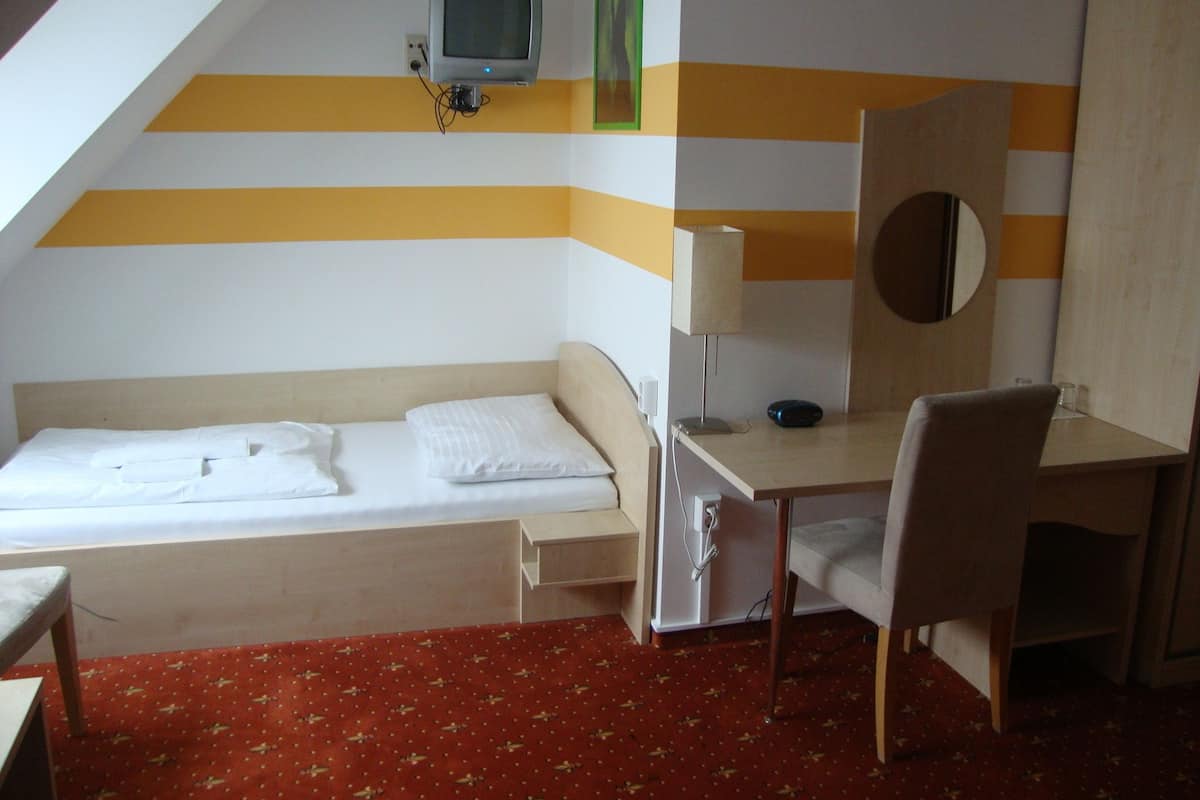 A small, single-bed room with a desk, chair, and a television mounted on the wall.