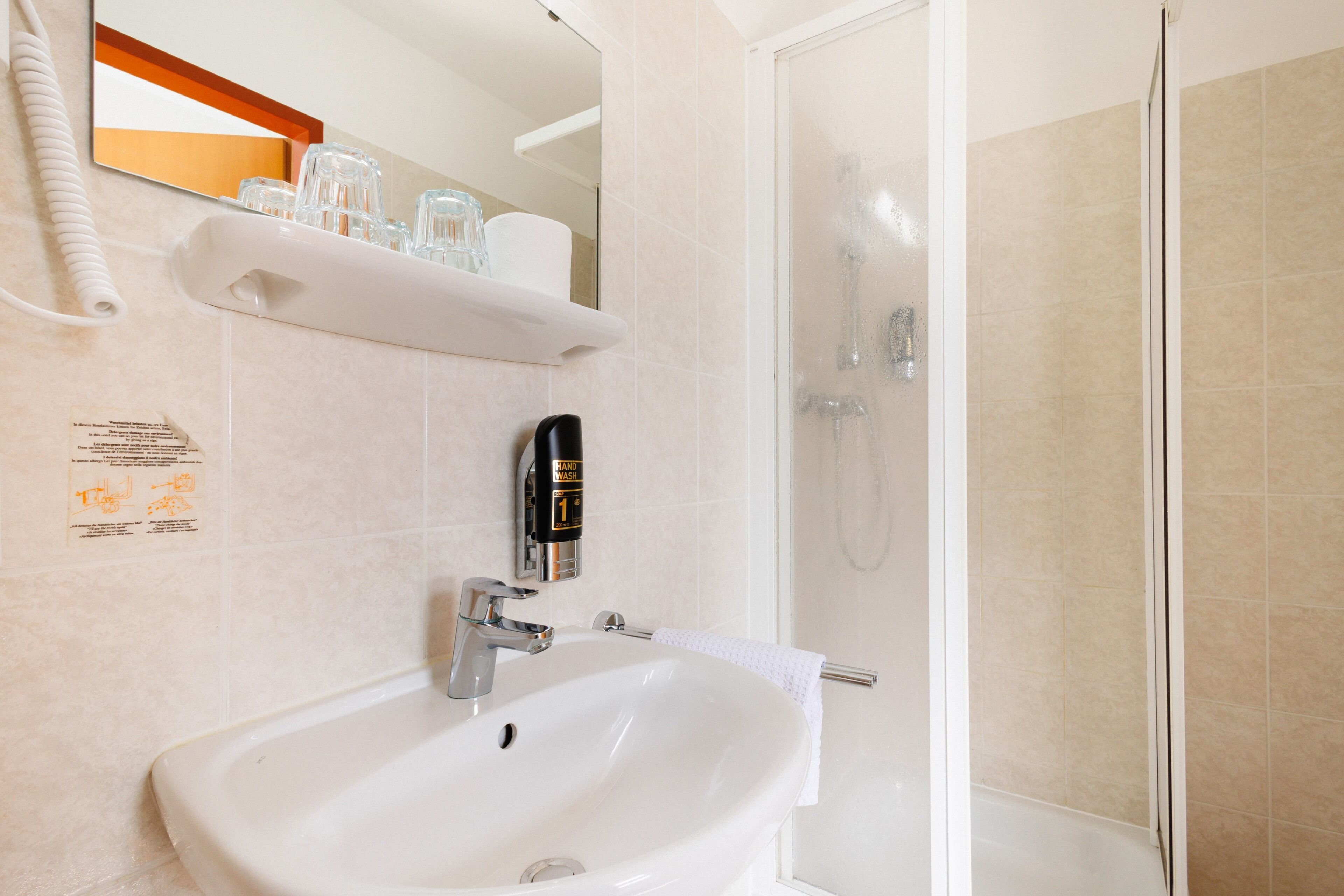 A bathroom with a white sink, a hand soap dispenser, a glass shower enclosure, and a towel rack.