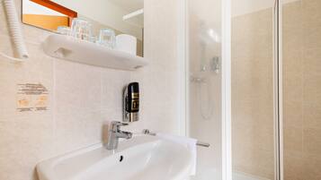 A bathroom with a white sink, a hand soap dispenser, a glass shower enclosure, and a towel rack.
