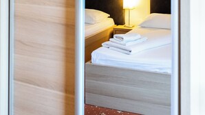 A hotel room with a sliding door, a bed with white linens, a nightstand with a lamp, and a wall with a yellow stripe.