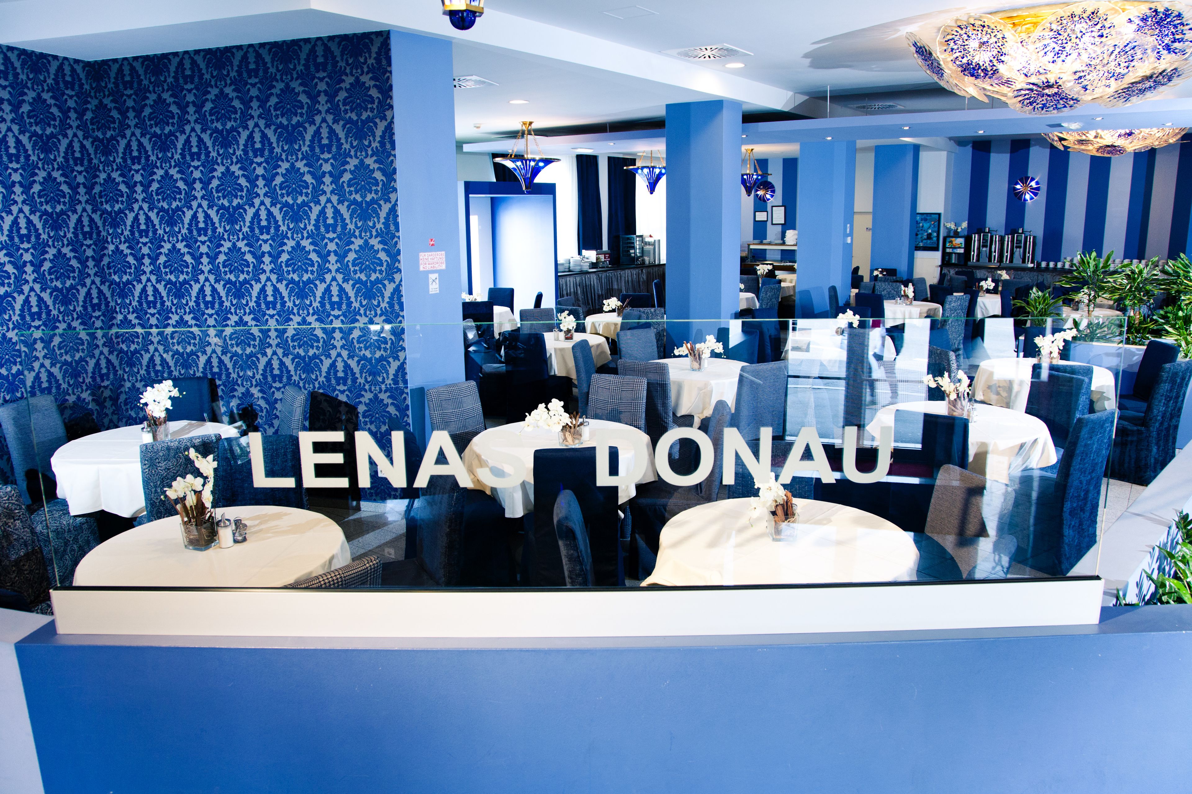 A modern restaurant interior with blue patterned walls, round tables, and comfortable seating.