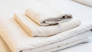 Ein ordentlich bezogenes Bett mit gefalteten weißen Handtüchern und Kissen, ein hölzernes Kopfende und eine leuchtend gelbe Wand.