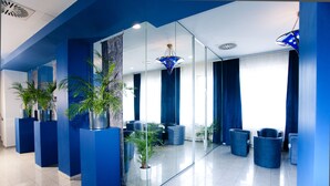 A modern lobby with blue walls, glass partitions, and seating areas.
