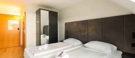 Quarto de hotel com duas camas, piso de madeira, cabeceira escura e um espelho.