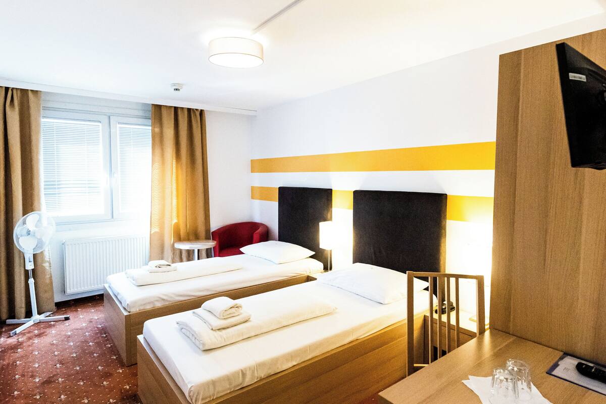 A hotel room with two beds, a desk, a chair, a TV, and a window with curtains.
