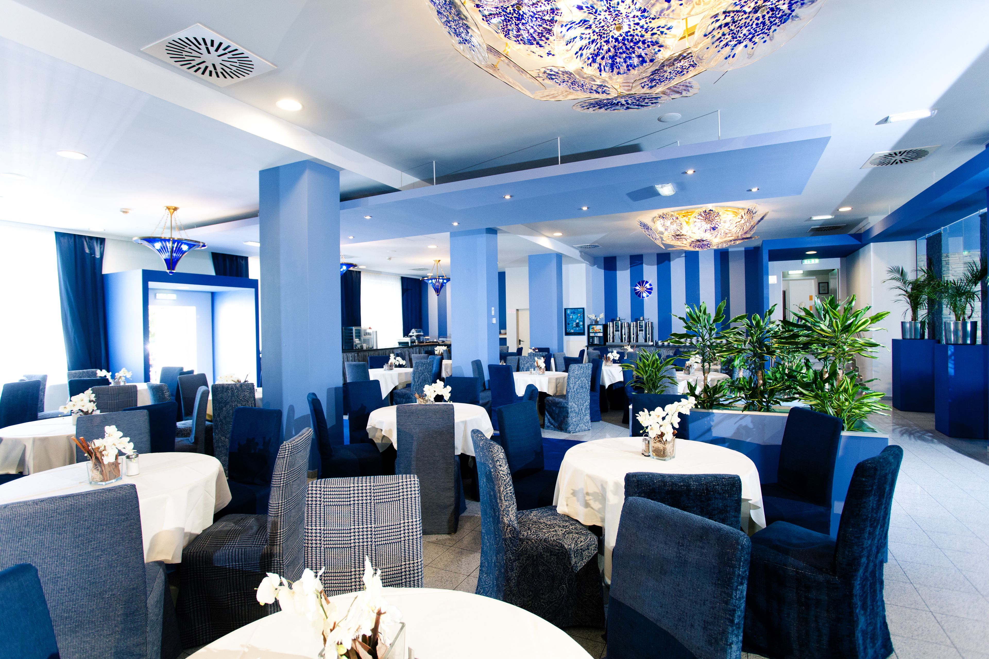 Un comedor moderno con mesas redondas, sillas tapizadas en azul y lámparas decorativas en el techo.