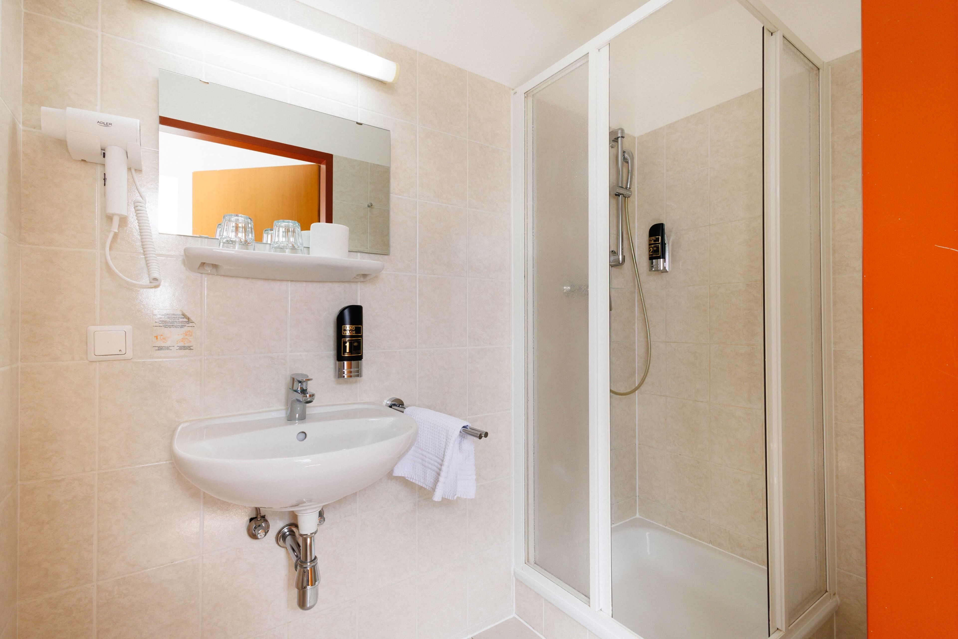 A bathroom with a sink, mirror, towel rack, and a shower area.