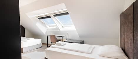A bedroom with a sloped ceiling, skylight, a bed, a chair, and a desk.
